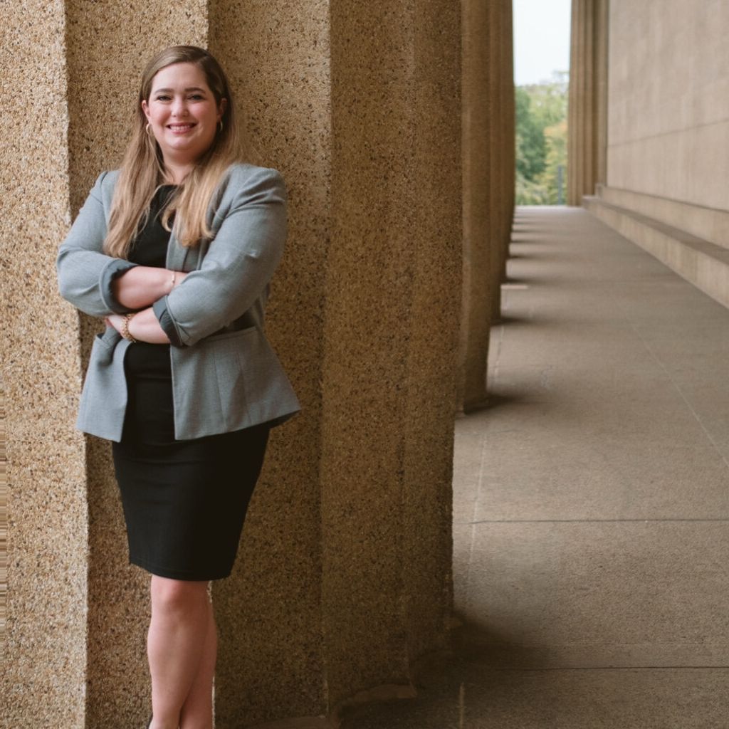 Professional woman in business attire standing confidently by stone columns.