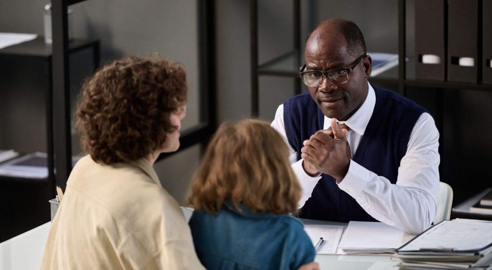 a man sitting at a desk talking to a woman that is holding a child
