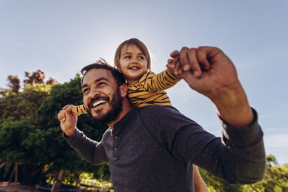 Father and child enjoying a piggyback ride in the park on a sunny day.