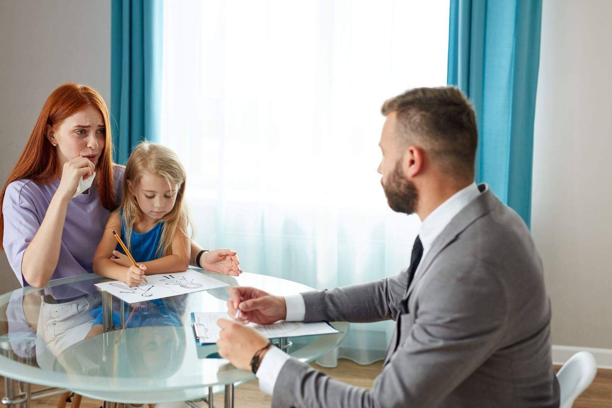 a woman sitting at a table with a little girl, she is talking to a lawyer